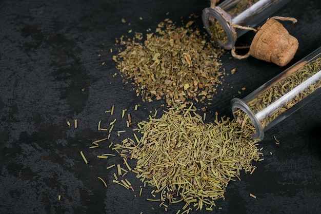 Assorted spices and herbs on dark black background. Seasonings for food. Rosemary and basil in glass flasks. Homemade spices ingredients for cooking