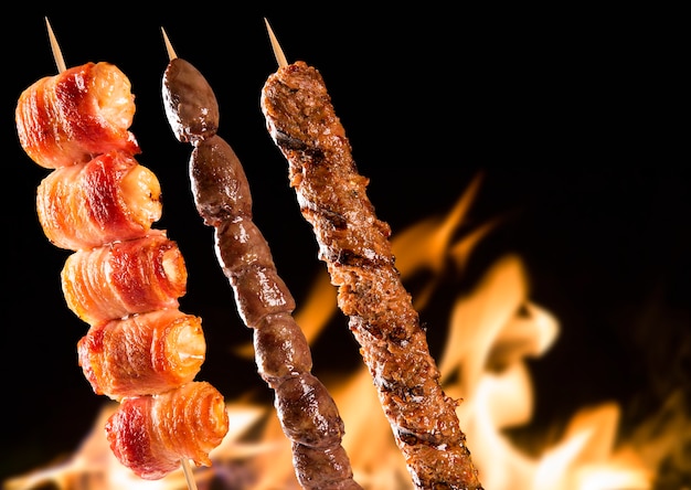 Assorted steak skewers over fire flames.