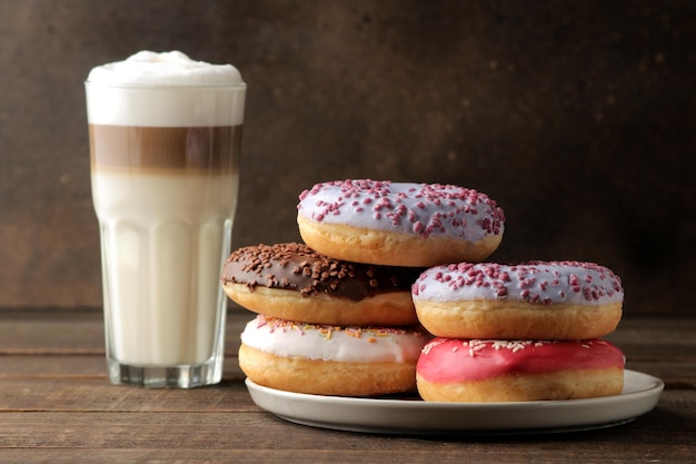 Assorted sweet donuts with icing and toppings and coffee latte on a brown wooden table