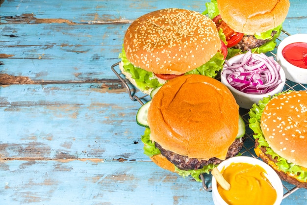 Assorted traditional American burgers, with sauces and fries on a wooden blue background