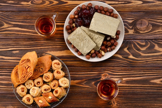 Assorted traditional eastern desserts with tea on wooden background. Arabian sweets on wooden table. Baklava, halva, rahat lokum, sherbet, nuts, dates, kadayif on plates. Space for text.