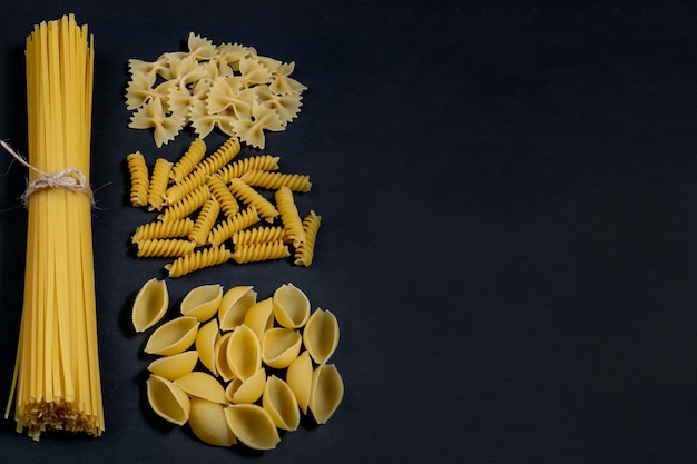 Assorted types of pasta on black table. Top view. Various forms of pasta. Copy space for design.