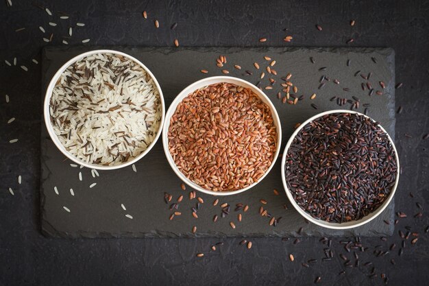 Assortimento di varietà di riso gourmet in ciotole su sfondo nero. vista dall'alto.