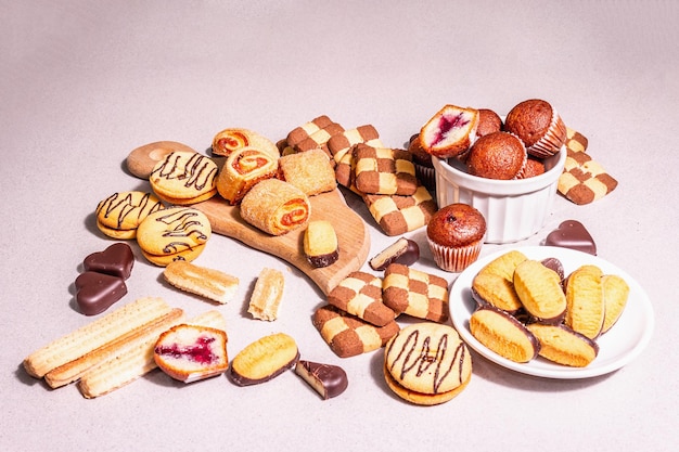 Assorted various cookies and muffins. Fashionable hard light, dark shadow. Stone concrete background, close up