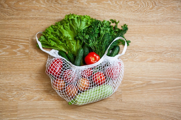 Assorted vegetables in grocery mesh string bag on wooden background