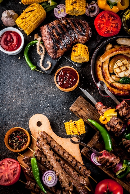 Assortiment diverse barbecue gerechten grill vlees, bbq party fest - shish kebab, worstjes, gegrilde vleesfilet, verse groenten, sauzen, kruiden, donkere roestige betonnen tafel, boven exemplaarruimte