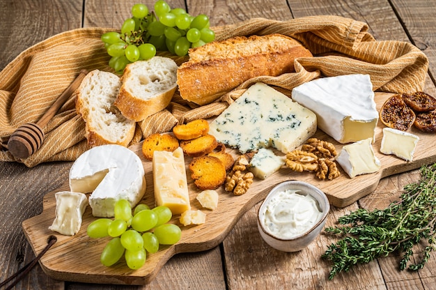 Assortiment Kaas Brie, Camembert, Roquefort, Parmezaanse kaas, blauwe roomkaas met druif, vijg, brood en noten. houten achtergrond. Bovenaanzicht.