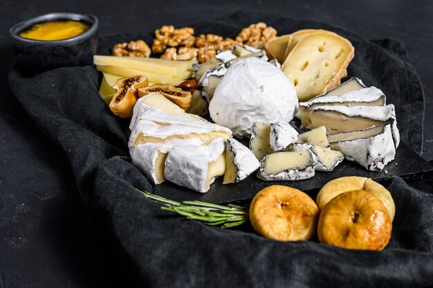 Assortiment van Franse kaas met honing, noten en vijgen op snijplank. Zwarte achtergrond. Bovenaanzicht