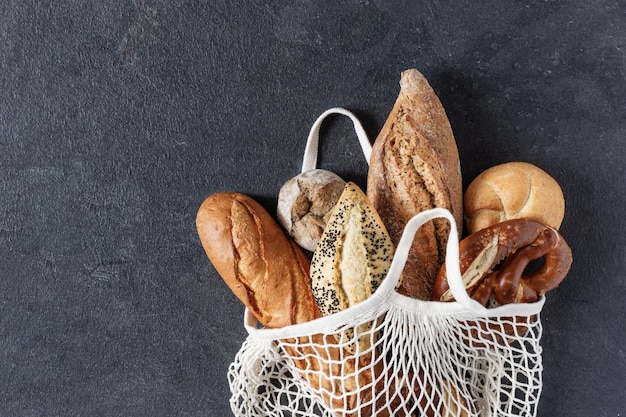 Assortiment van gebakken brood en broodjes in witte mesh draagtas op zwarte achtergrond bovenaanzicht