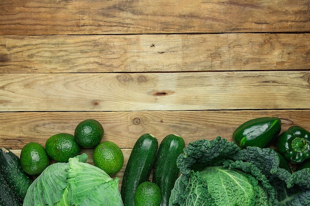 Assortiment van groene groenten gerangschikt in onderste rand op plank houten achtergrond.