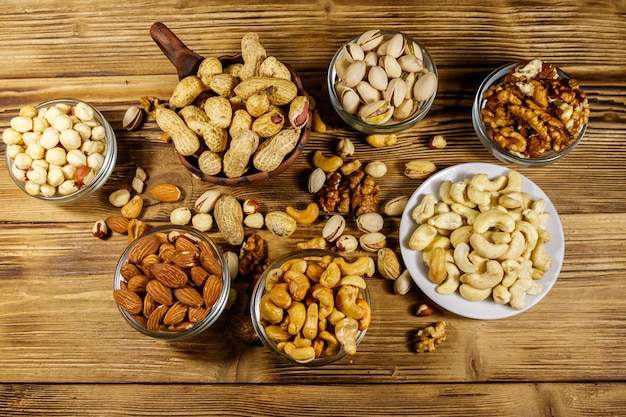 Assortiment van noten op houten tafel Amandel hazelnoot pistache pinda walnoot en cashewnoten in kleine kommen Bovenaanzicht Gezond eten concept