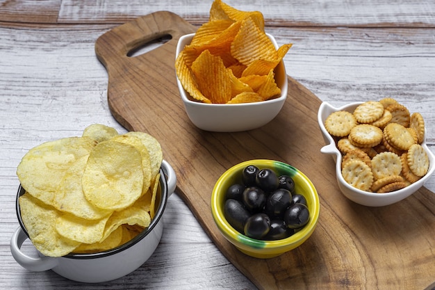 Assortiment van snacks thuis met chips, bier, crackers, groene en zwarte olijven op houten tafel