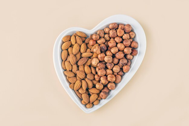 Assortiment van verschillende soorten noten - hazelnoten, amandelen in hartvormige plaat op pastel achtergrond.
