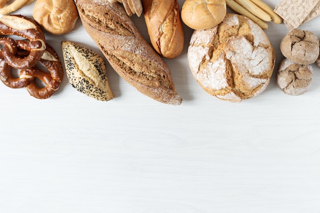 Ассортимент печеного хлеба и булочек на белом деревянном фоне вид сверху Здоровый органический хлеб
