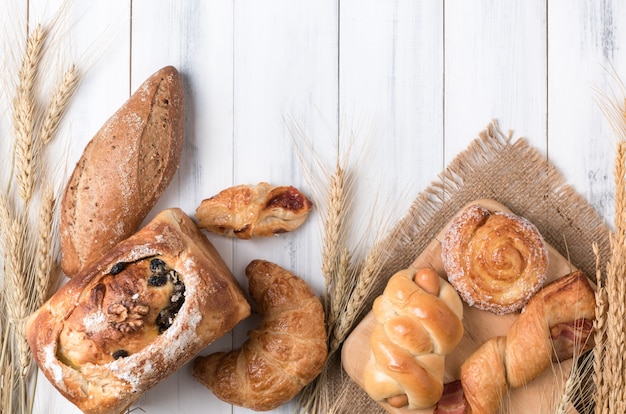 Assortment of baked bread and wheat on white wood table