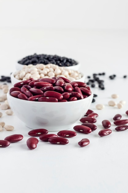 Assortment of beans in a white bowl on white background. Red kidney beans, white beans and black beans