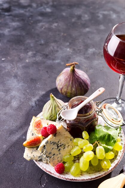 Assortment of cheese, berries and grapes with red wine in glasses on stone surface