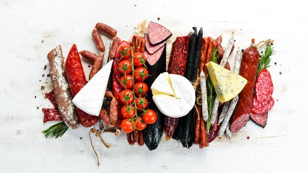 Assortment of cheese dried salami and smoked sausages on a white wooden background Top view Free space for your text