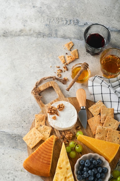 Assortment of cheese honey cracker blueberries grapes with red and white wine in glasses antipasto server on white marble board on grey background Cheese plate Flat lay copy space