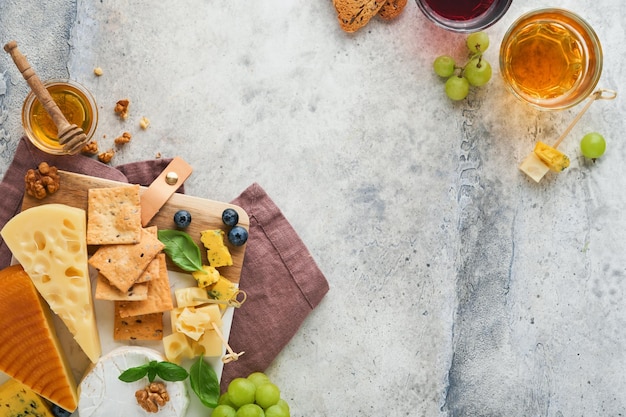 Assortment of cheese honey cracker blueberries grapes with red and white wine in glasses antipasto server on white marble board on grey background Flat lay copy space