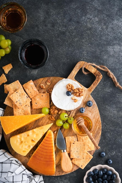 Assortment of cheese honey cracker blueberries grapes with red and white wine in glasses antipasto server on white marble board on old dark grey background Flat lay copy space