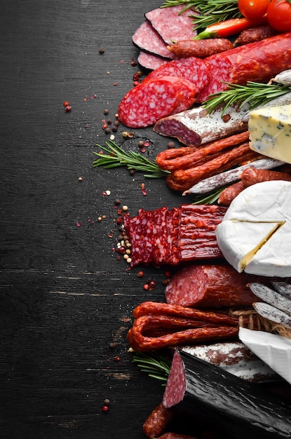 Assortment of cheese salami sausage spices and meat products on black background Top view Free space for your text