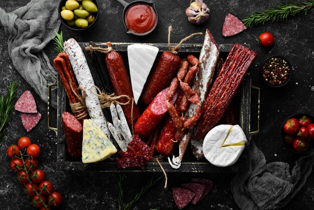 Assortment of cheese salami sausage spices and meat products on black background Top view Free space for your text