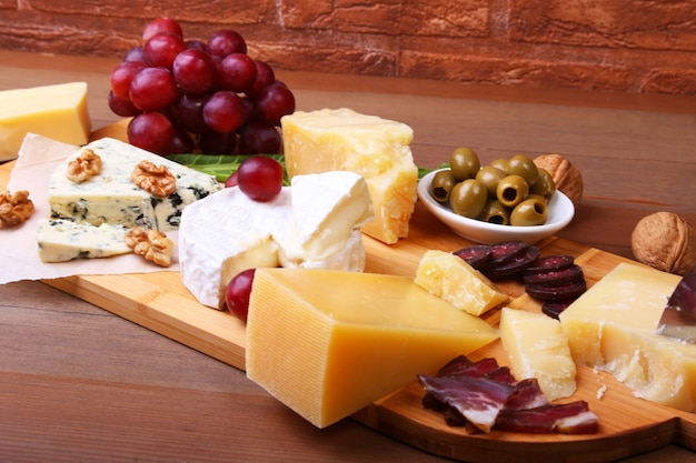 Assortment of cheese with fruits, grapes, nuts and cheese knife on a wooden serving tray.