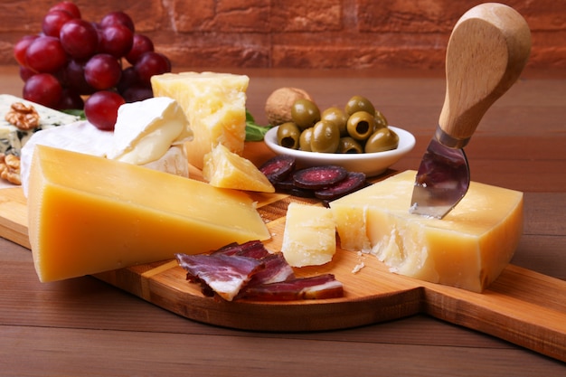 Assortment of cheese with fruits, grapes, nuts and cheese knife on a wooden serving tray.