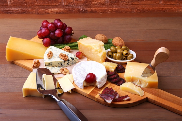 Assortment of cheese with fruits, grapes, nuts and cheese knife on a wooden serving tray.