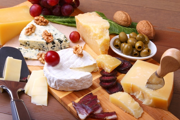 Assortment of cheese with fruits, grapes, nuts and cheese knife on a wooden serving tray.