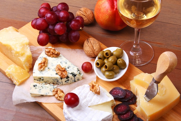 Assortment of cheese with fruits, grapes, nuts and cheese knife on a wooden serving tray.