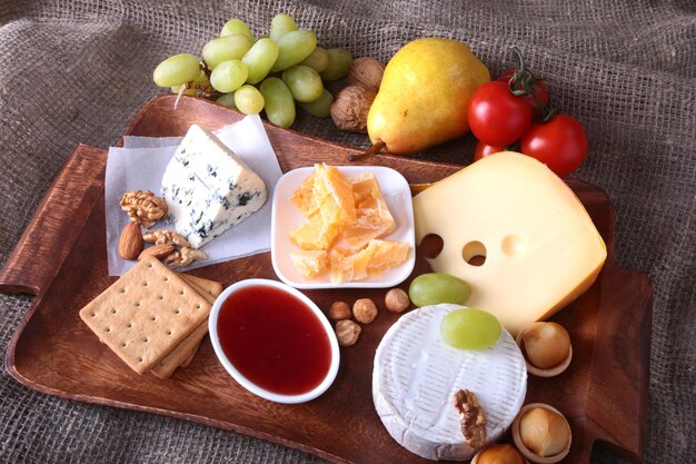 Assortment of cheese with fruits, grapes and nuts on a wooden serving tray.