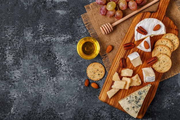 Assortment of cheese with honey, nuts and grape on a cutting board.