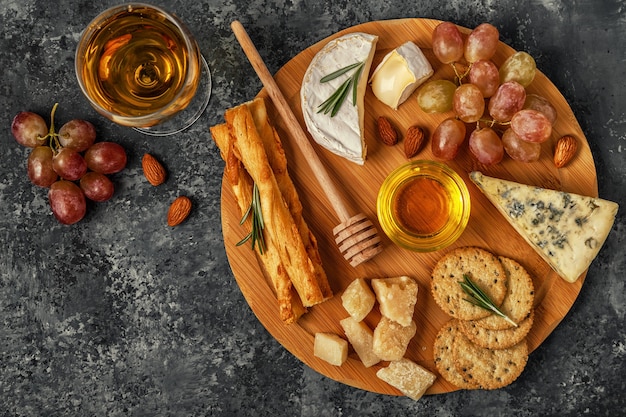 Assortment of cheese with wine, honey, nuts and grape on a cutting board, top view.