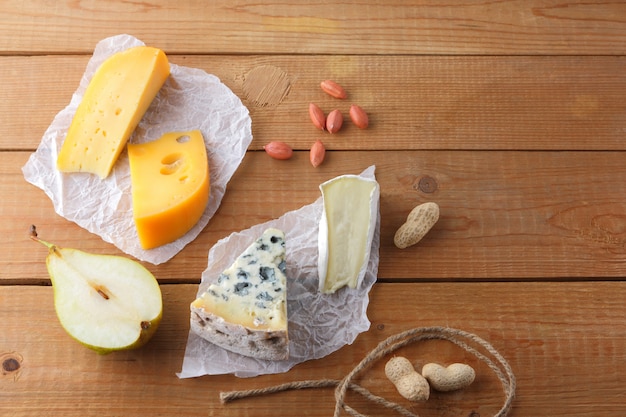 Assortment of cheeses, pears and peanuts on parchment paper. Camembert, hard yellow cheese, dorblu on wooden boards. Dairy products, half pears and nuts