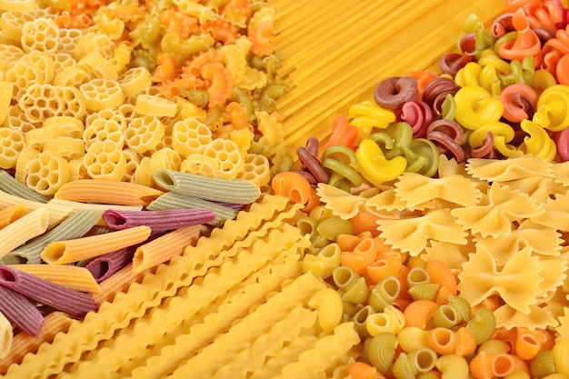 Assortment of colored uncooked Italian pasta close up as background