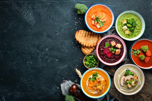 Assortment of colored vegetable cream soups Dietary food On a black stone background Top view Free copy space