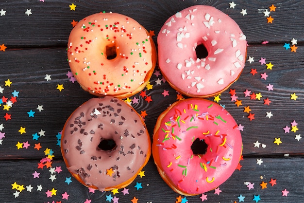 Assortment of colorful donuts decorated with colorful confetti sprinkles on dark wooden surface 