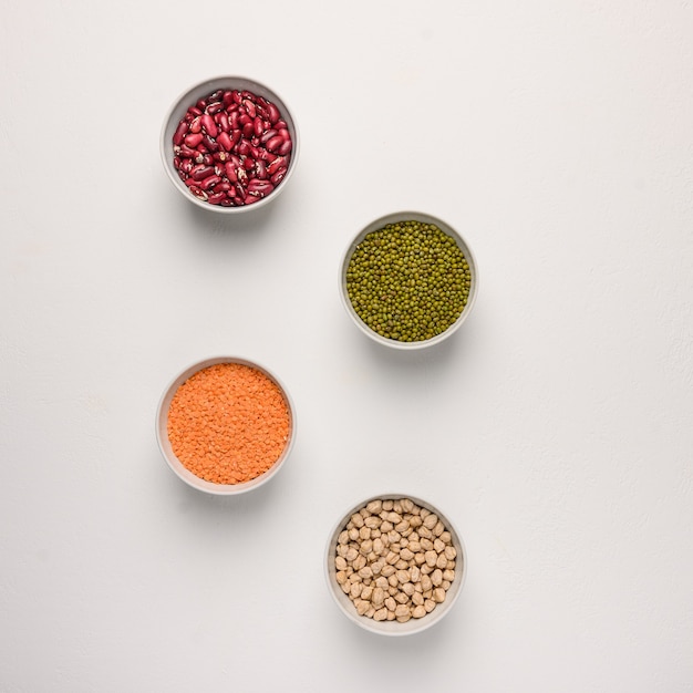 Assortment of colorful legumes in bowls lentils beans chickpeas mash on concrete surface top view