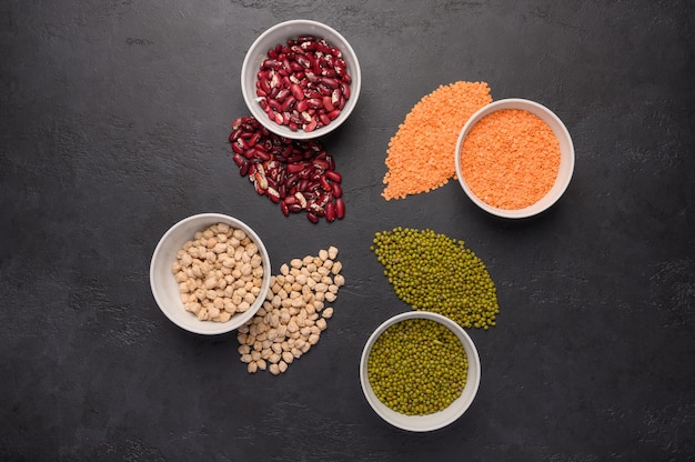 Assortment of colorful legumes in bowls lentils beans chickpeas mash on concrete surface top view