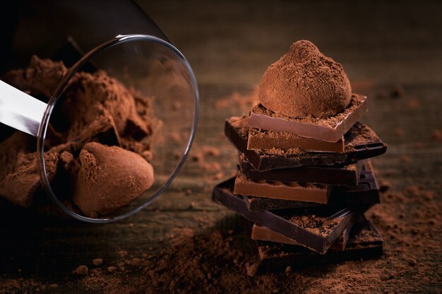 Assortimento di pile di cioccolato fondente e al latte, tartufi. dolci al bicchiere. cioccolato con cacao in polvere scuro sul tavolo in legno rustico. messa a fuoco macro selettiva. dolci e sfondo di cioccolato.