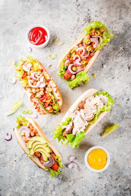 Assortment of different homemade vegan carrot hot dogs, with fried onion, avocado, chili, mushrooms, tomatoes and beans, grey stone  copyspace top view