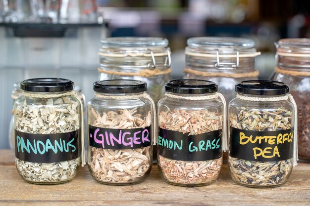 Assortment of dried spices in glass bottles on wooden background. Dry ginger, pandanus, lemon grass and butterfly pea in glass jars, close up