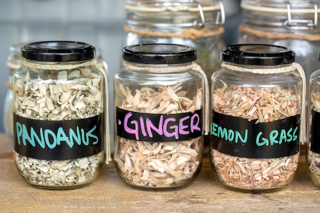 Assortment of dried spices in glass bottles on wooden background. Dry ginger, pandanus, lemon grass in glass jars, close up