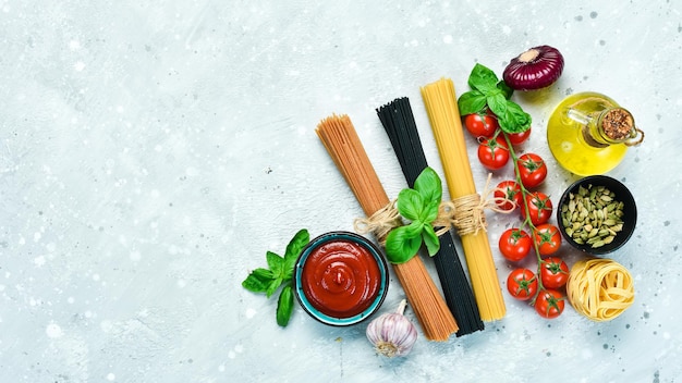 Assortment of dry colorful spaghetti and pasta with cherry tomatoes and ingredients, on a gray stone background. Dry pasta. Top view. Free space for text.