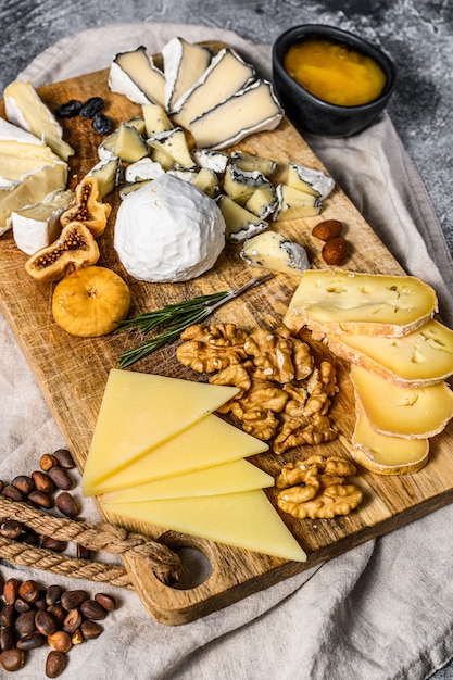 Assortment of French cheese with honey, nuts and figs on cutting board. Gray background. Top view.