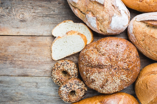 Assortment of fresh baked bread and buns on wooden table background, top view