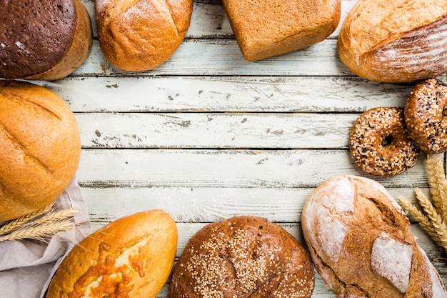 Assortment of fresh baked bread and buns on wooden table background, top view