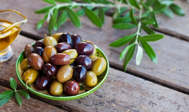 Assortment of fresh olives on a plate with olive tree brunches Wooden background Close up Copy space